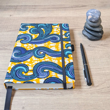 gold and blue wellness journal for self-care journaling with pen and stack of pebbles