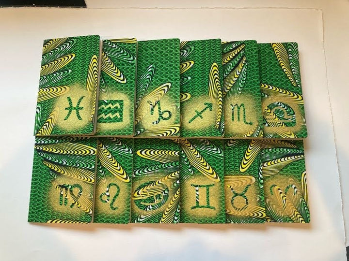 Virgo Season Journals for self-care journaling. 12 green journals with the different Zodiac signs stenciled on them in gold paint.
