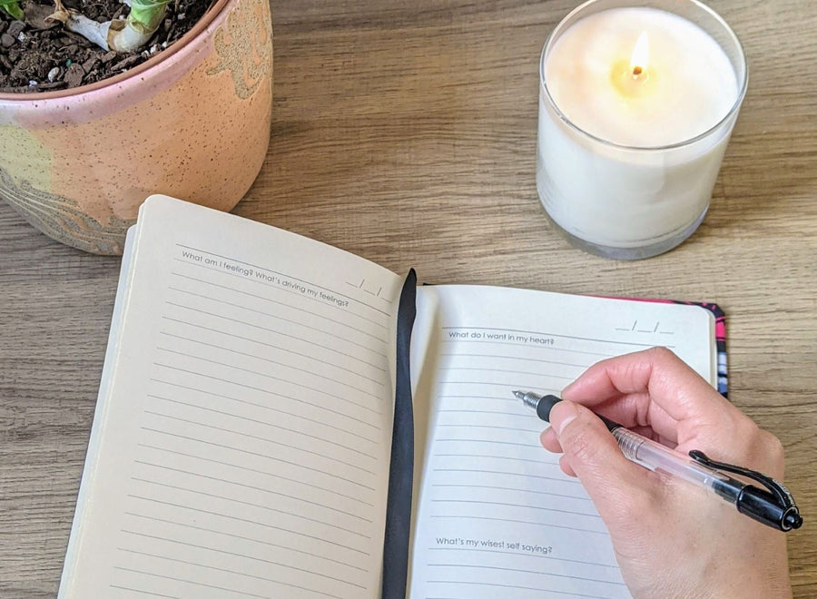 Hand self care journaling in custom wellness journal, with candle and plant